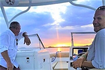 Two men seated on the back of a boat, enjoying a serene sunset over the water.