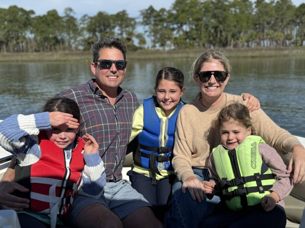 A family wearing life jackets enjoys a sunny day on a boat, smiling and embracing the adventure together.