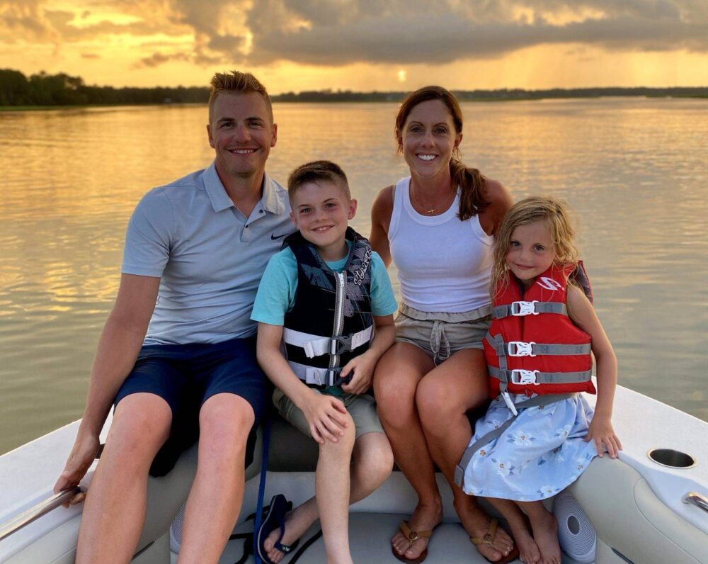 A family enjoying a serene boat ride together as the sun sets, casting warm hues across the sky and water.