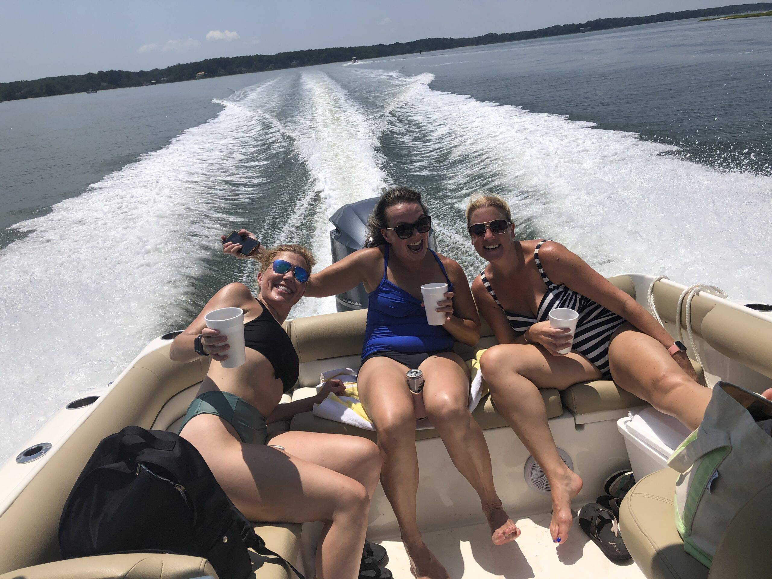 Three women enjoying a leisurely moment together on a boat, surrounded by calm waters and a clear sky.