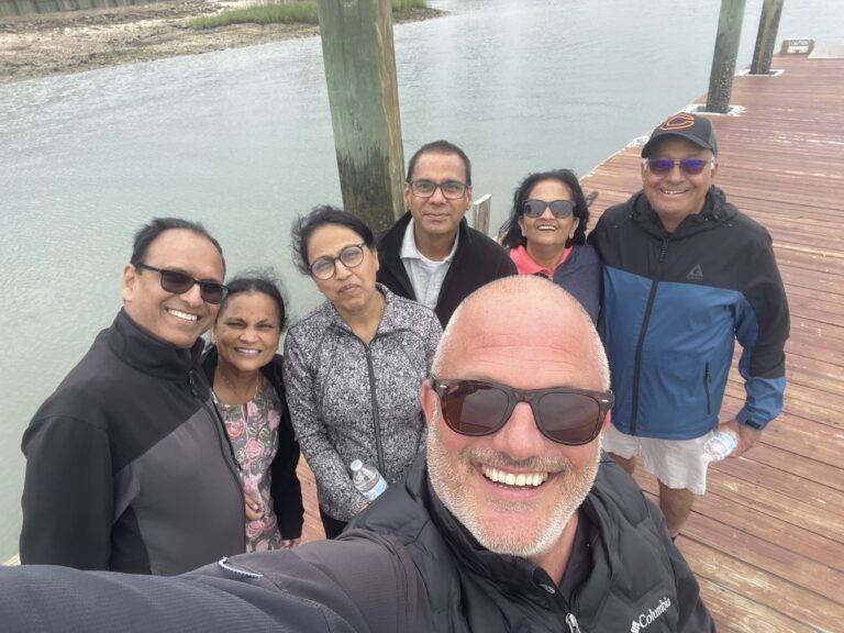 A group of friends smiling and posing for a selfie on a sunny dock, capturing a joyful moment together.