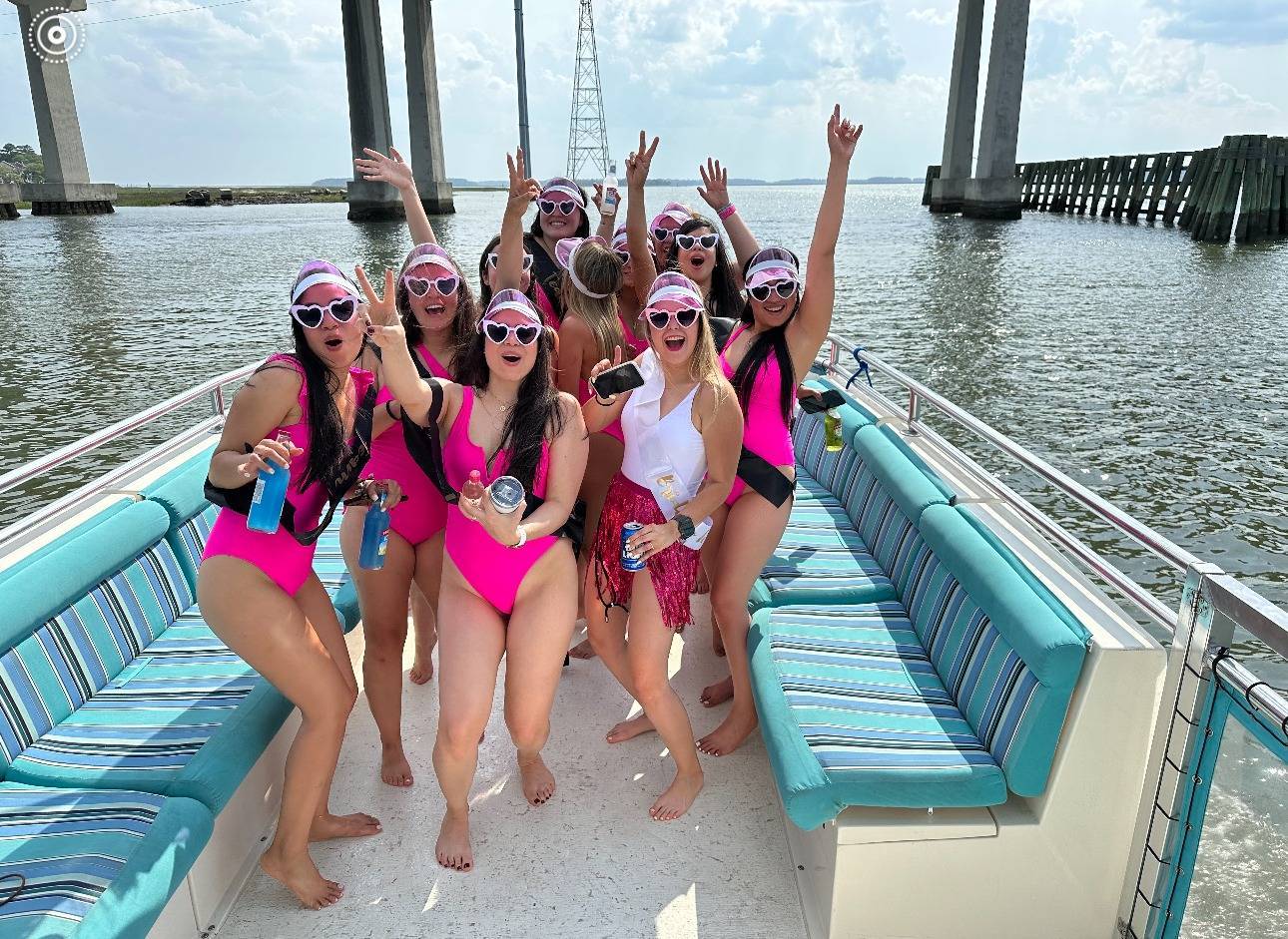 A group of women wearing pink swimsuits enjoying a sunny day on a boat, smiling and relaxing together.