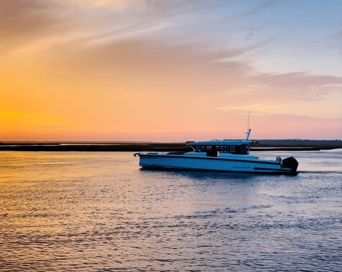 A boat glides across the water, silhouetted against a vibrant sunset sky filled with warm hues of orange and pink.